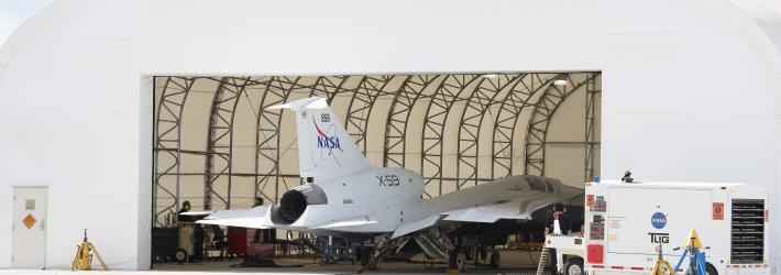 A white airplane sits inside of a white hangar with its nose facing inward.