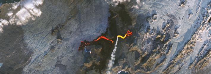 Lava cuts a jagged orange gash across a grayish landscape in this satellite view of Iceland's Reykjanes peninsula on Nov. 24, 2024. A plume of white smoke - gas - streams toward the bottom of the picture.